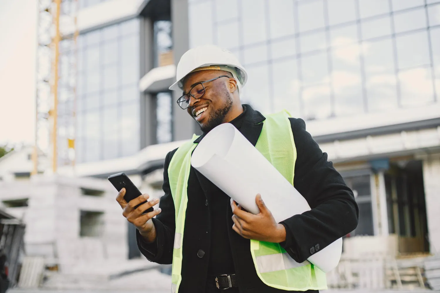 Site engineer in a hard hat and high-visibility vest holding drawings and a phone