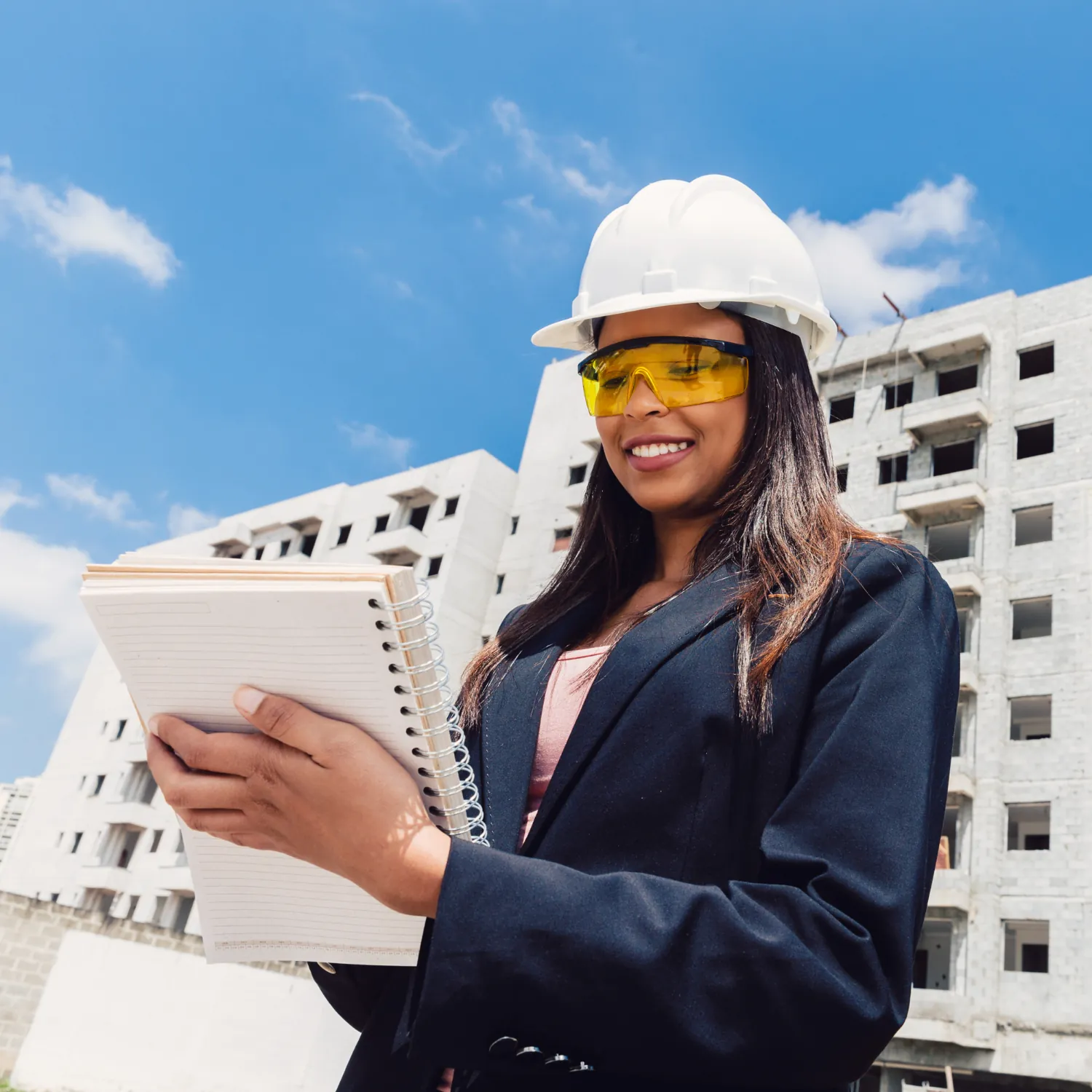 Engineer in safety glasses reviewing notes in front of a building under construction