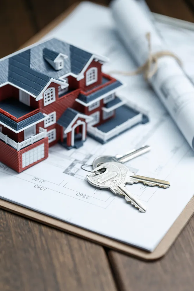 House keys resting on property plans beside a small model home